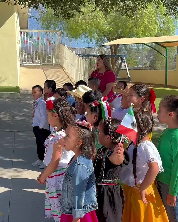 Niñas y niños con trajes típicos mexicanos y banderitas en el patio de Colegio Encinos