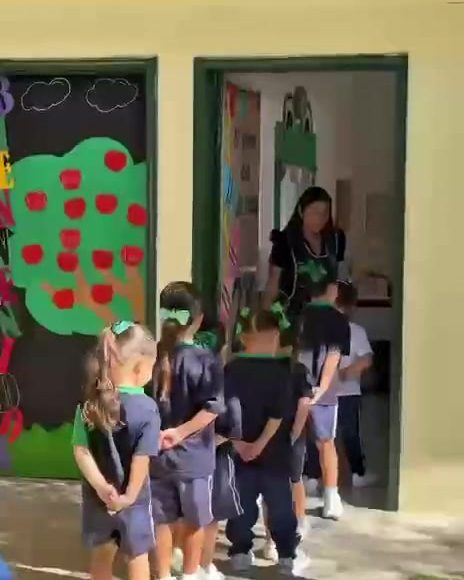 Alumnos formados en fila para entrar a su salón, decorado con un árbol de manzanas