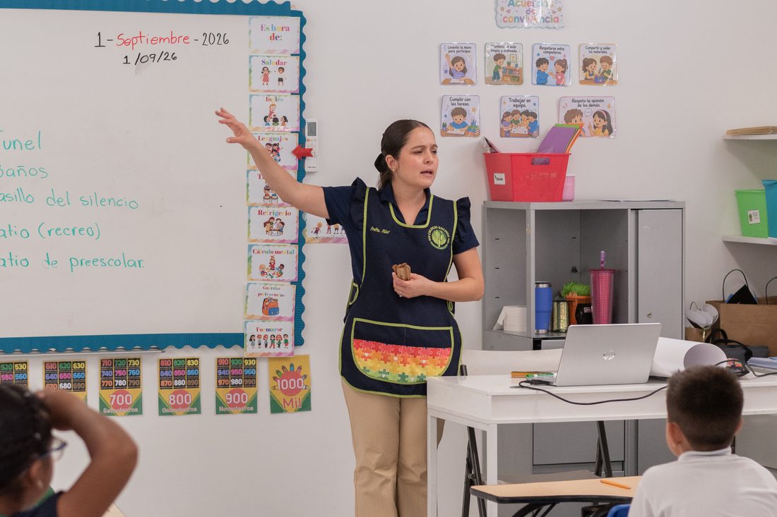 Maestra de primaria explicando frente al pizarrón a su grupo