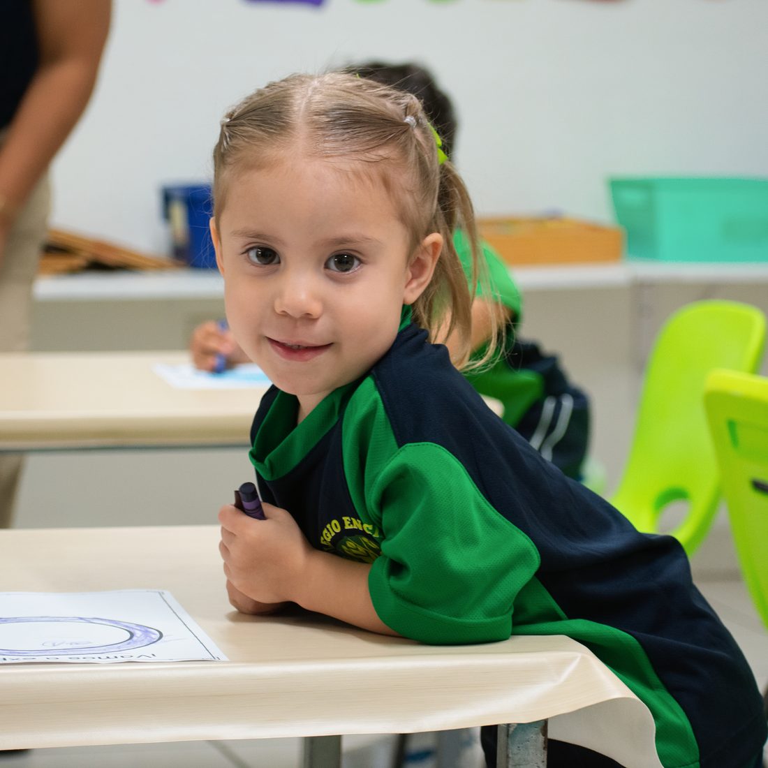 Niña de preescolar de Colegio Encinos sonriendo mientras trabaja en su mesa con un color en la mano