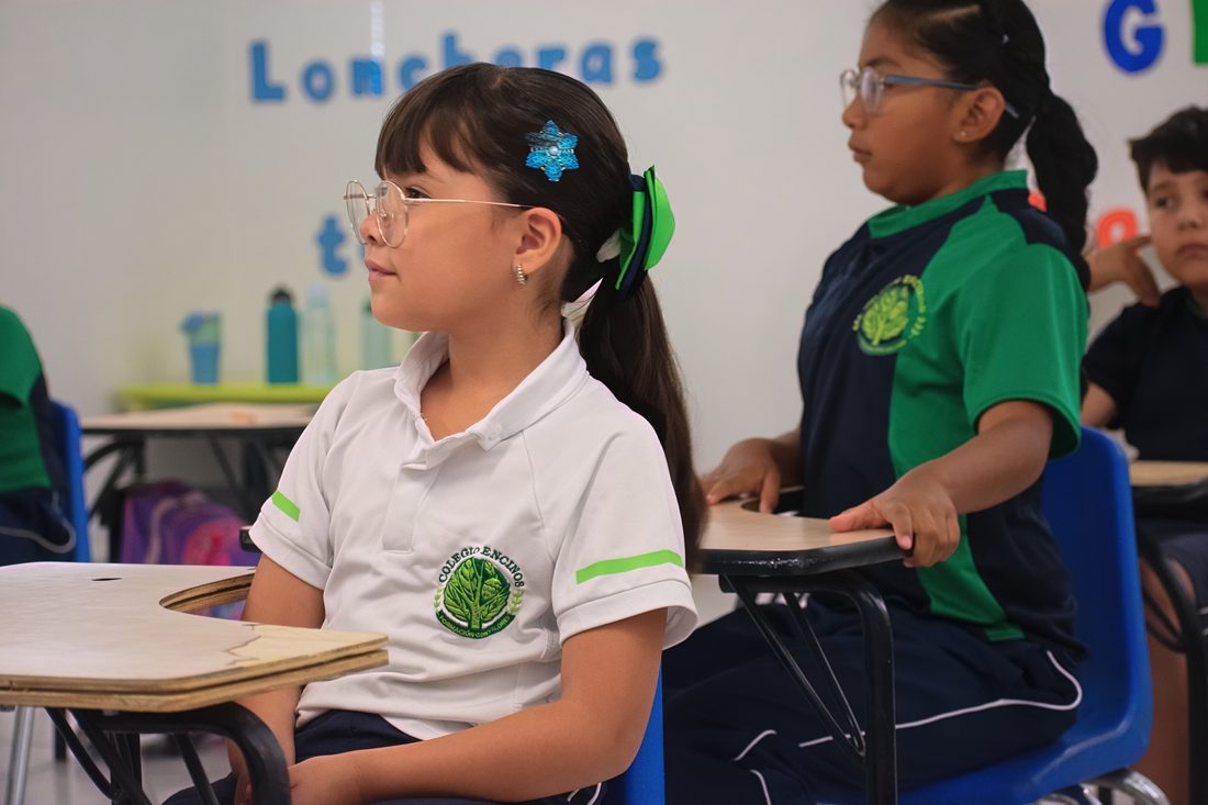 Elementary student with glasses working at her desk beside her classmates