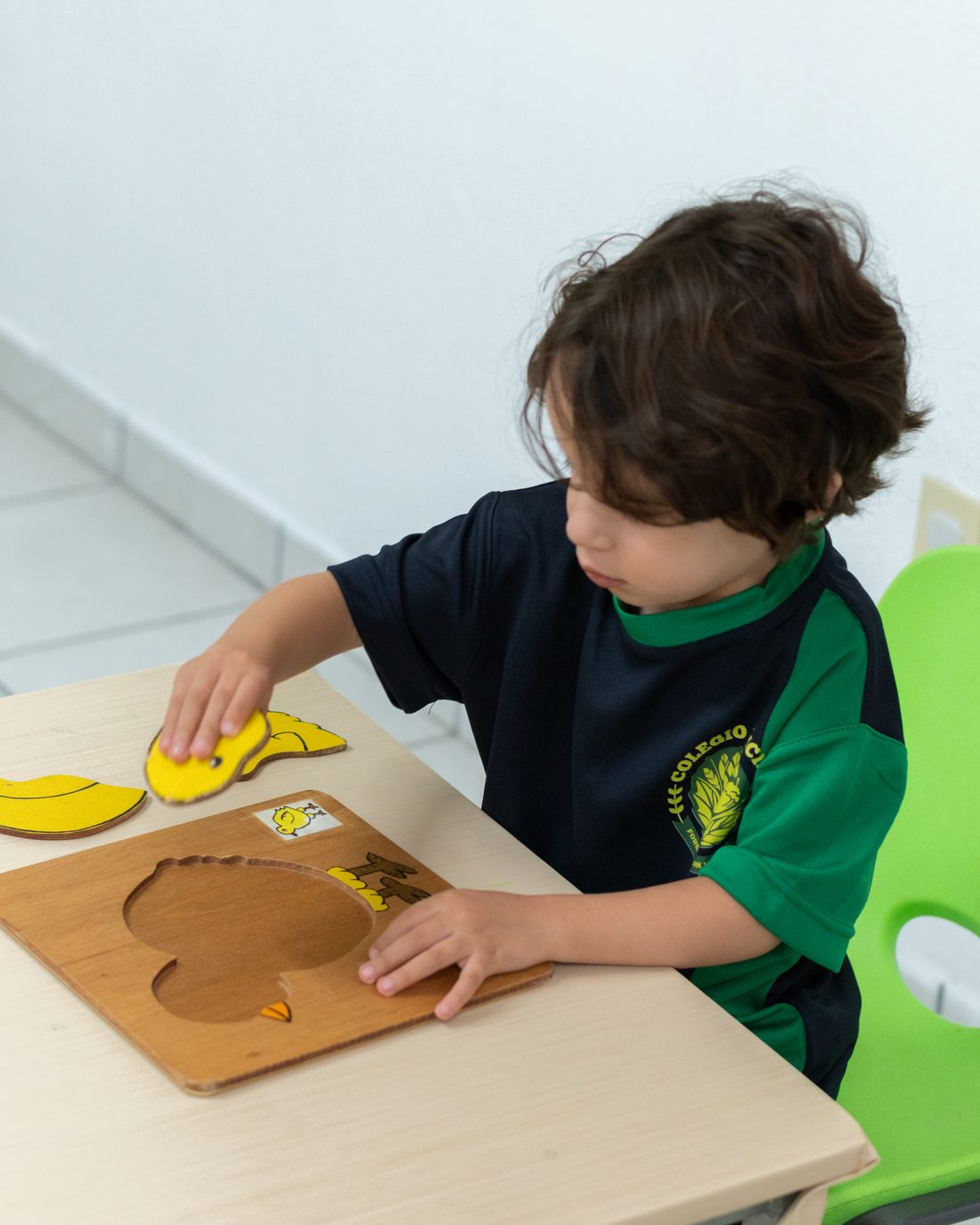 Preschool boy putting together a colorful wooden puzzle in the classroom