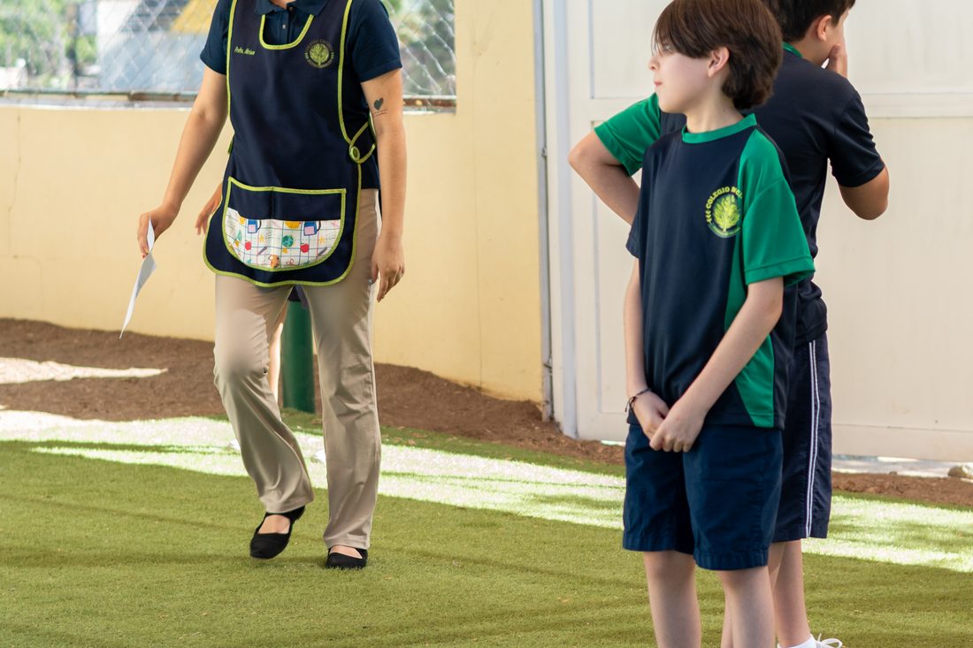 Maestra y alumnos de primaria en la cancha de pasto sintético del colegio, durante la clase de educación física