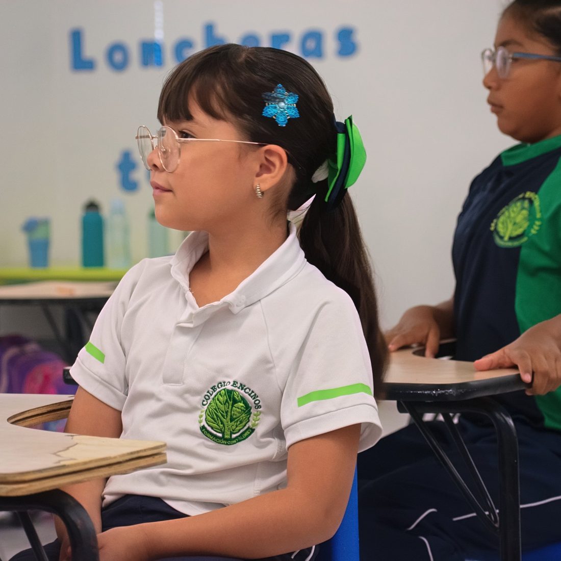 Alumnas de primaria de Colegio Encinos atentas en clase, con el uniforme blanco y verde del colegio